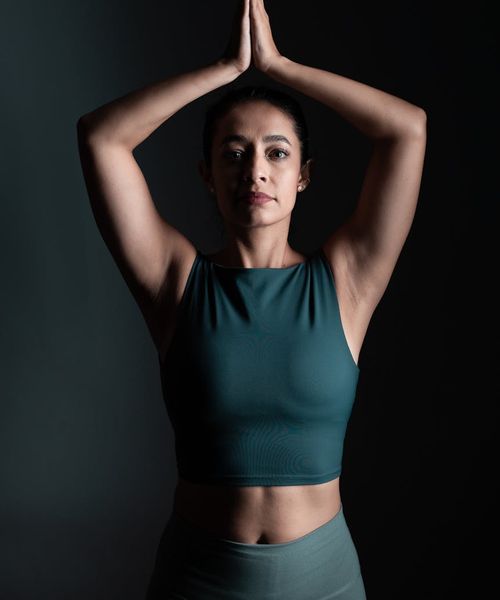 Woman in a peaceful yoga pose against a dark background with lilac light.